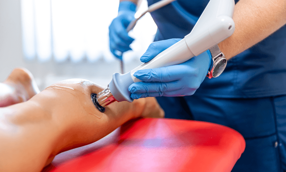 A healthcare professional using a therapeutic ultrasound device on a patient's knee, with blue gloves and a clinical setting background.