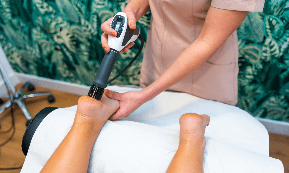 A therapist using a handheld device on a client's ankle, in a serene setting with tropical-patterned walls.